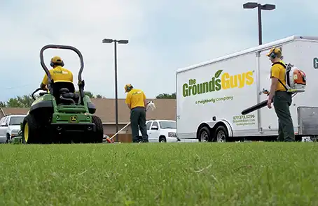 Three Grounds Guys associates performing lawn cleanup work next to a branded company trailer.