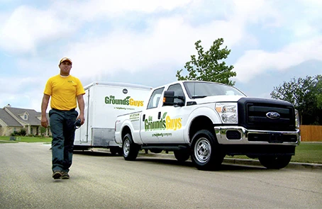 Grounds Guys employee walking next to truck and trailer