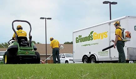 Three Grounds Guys employees performing lawn cleanup next to company trailer.