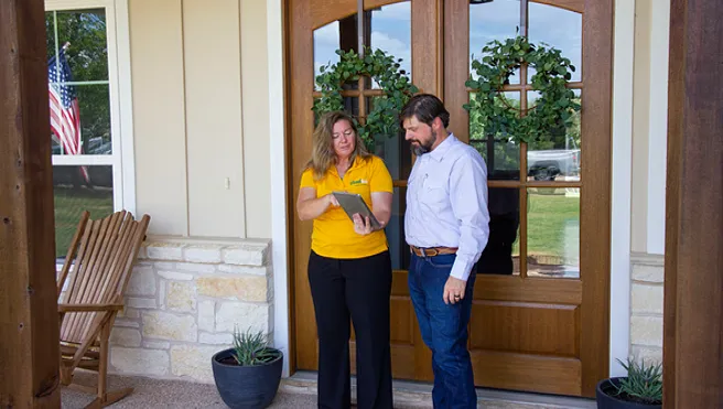 A service professional with The Grounds Guys standing with a client at his front door, showing him financing information on a tablet.
