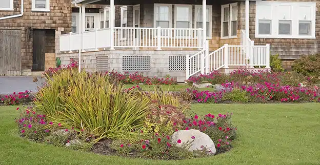 Flower beds with red impatiens in the front yard of a large home.