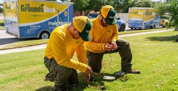 The Grounds Guys service professional watching water spray from sprinkler heads installed in a lawn.