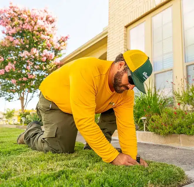The Grounds Guys service professional monitoring sprinklers as they spray water on a lawn.