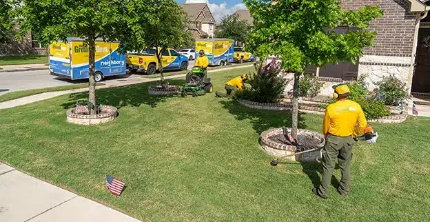 Three Grounds Guys service professionals mowing and edging a front lawn.