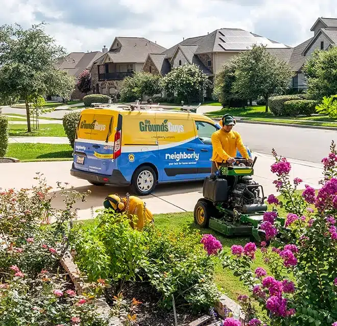 The Grounds Guys service professionals mowing and edging a front lawn.