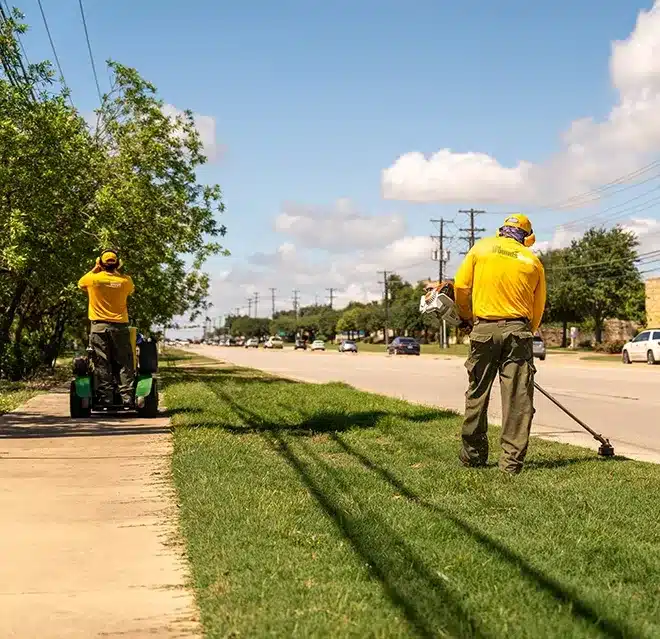 The Grounds Guys service professionals mowing and edging part of a commercial property's lawn.