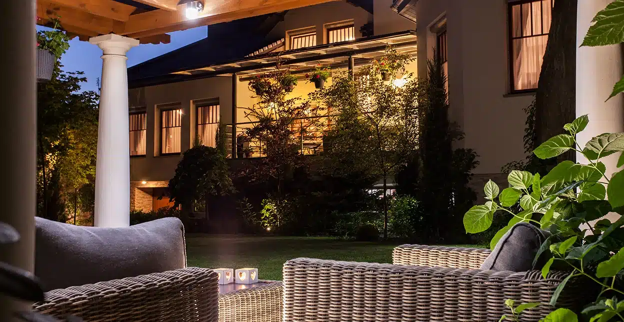 A backyard patio with pergola lit by outdoor lighting.