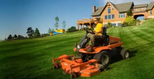 The Grounds Guys service professional mowing a large home's front lawn.