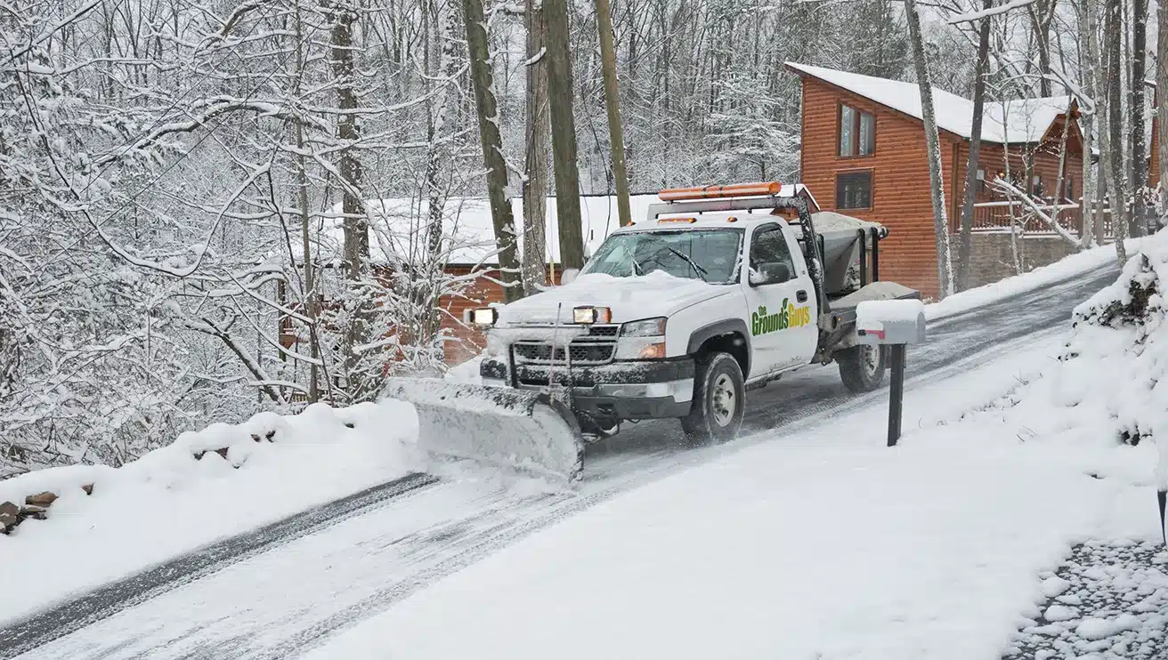The Grounds Guys truck with snow blade pushing snow off a sloped driveway.