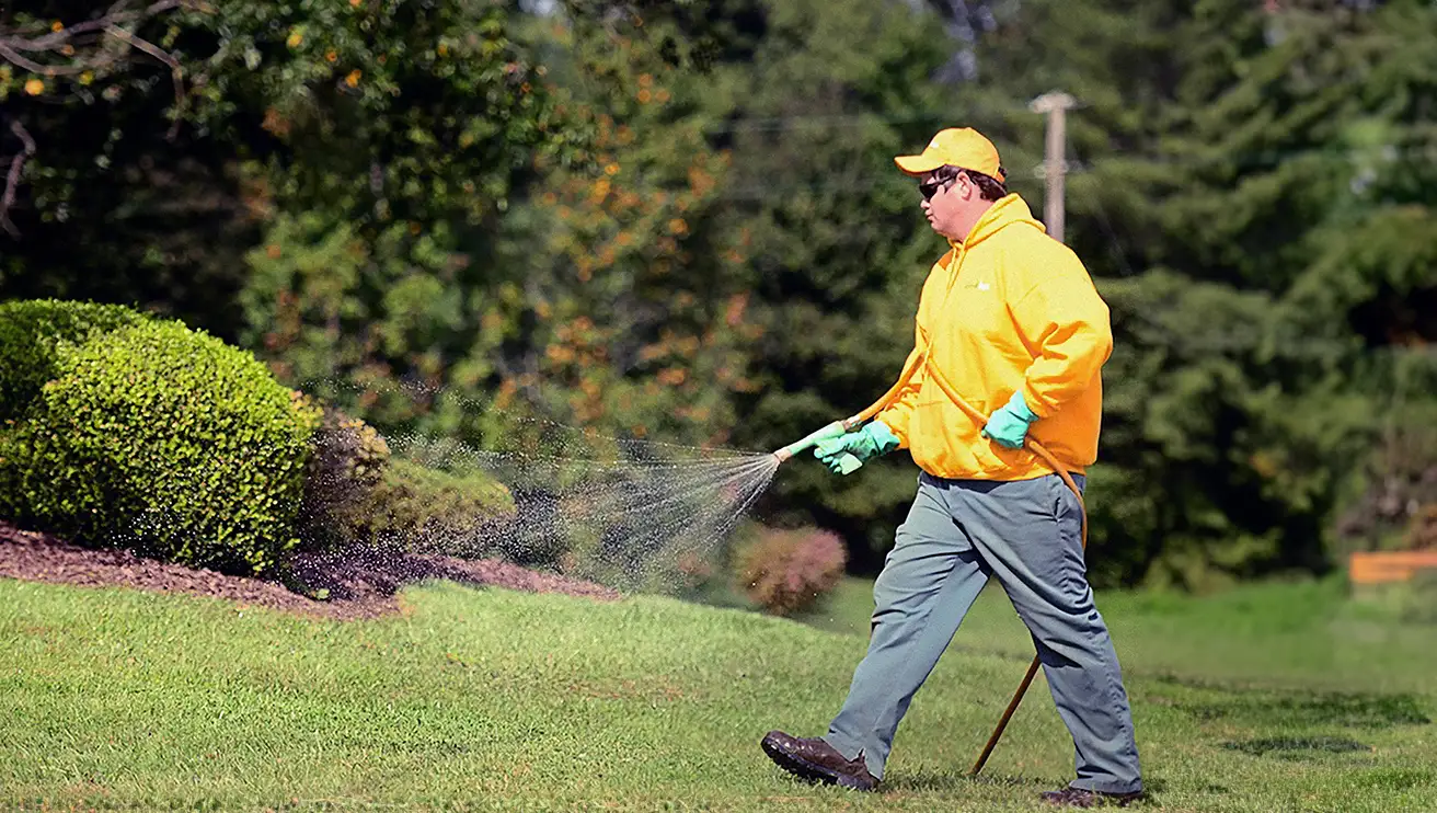 The Grounds Guys service professional spraying fertilizer on a lawn.