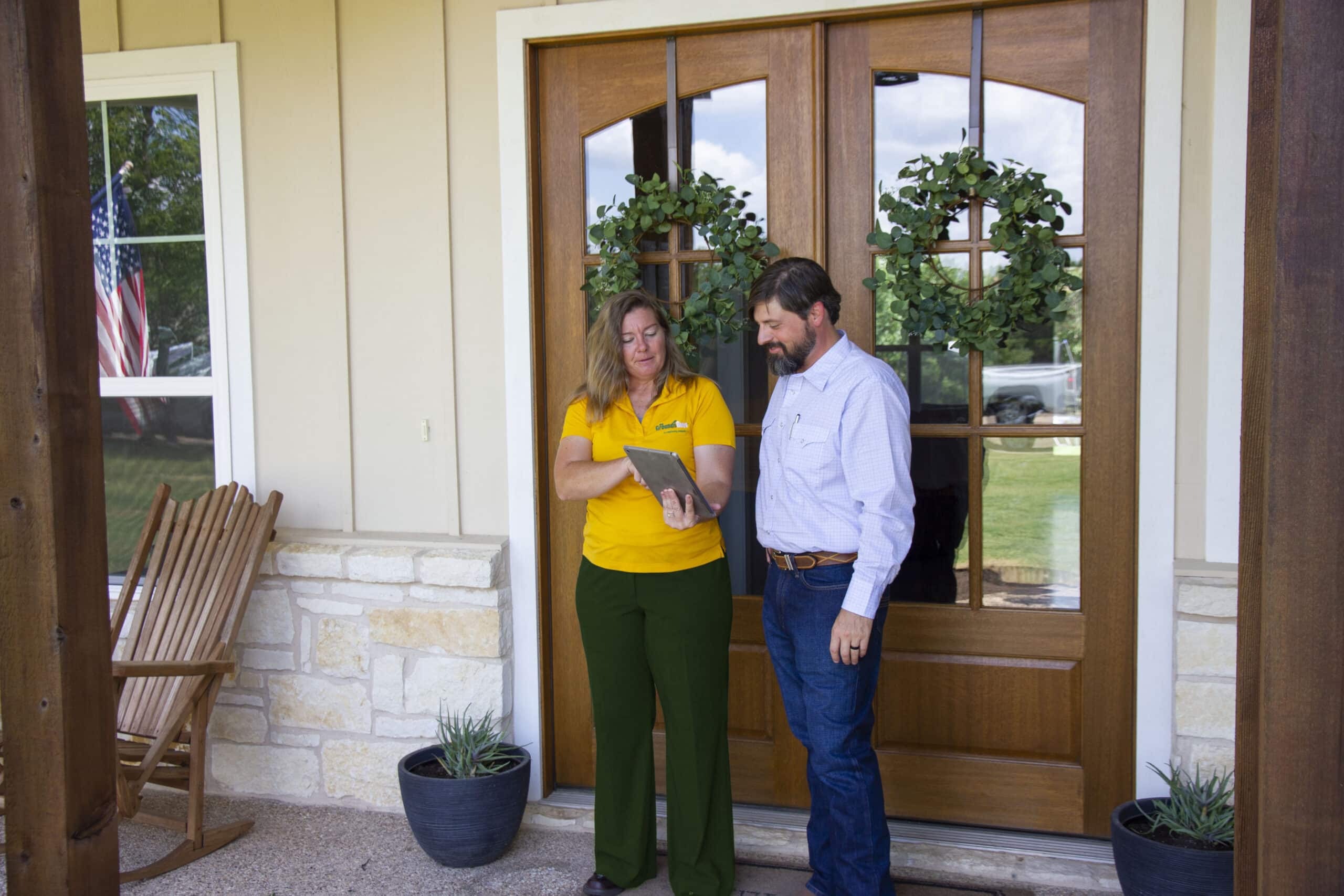 A Grounds Guys service professional standing with a client at his front door, showing him financing information on a tablet.
