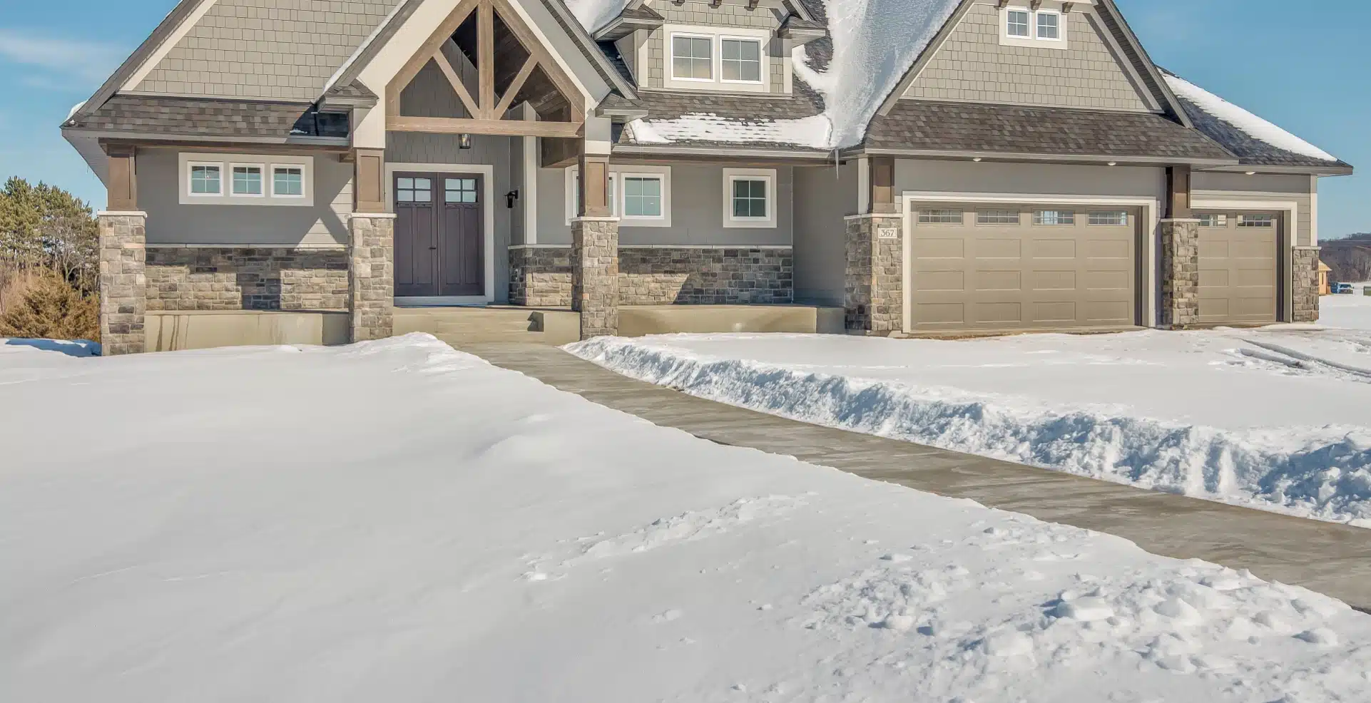 A large home on a clear winter day, with snow covering the ground except for the walkway to the front door, which has been meticulously cleared.