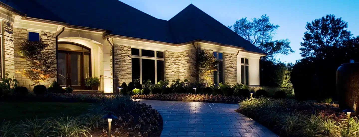 A large home at dusk with outdoor pathyway lights illuminating the brick walkway.