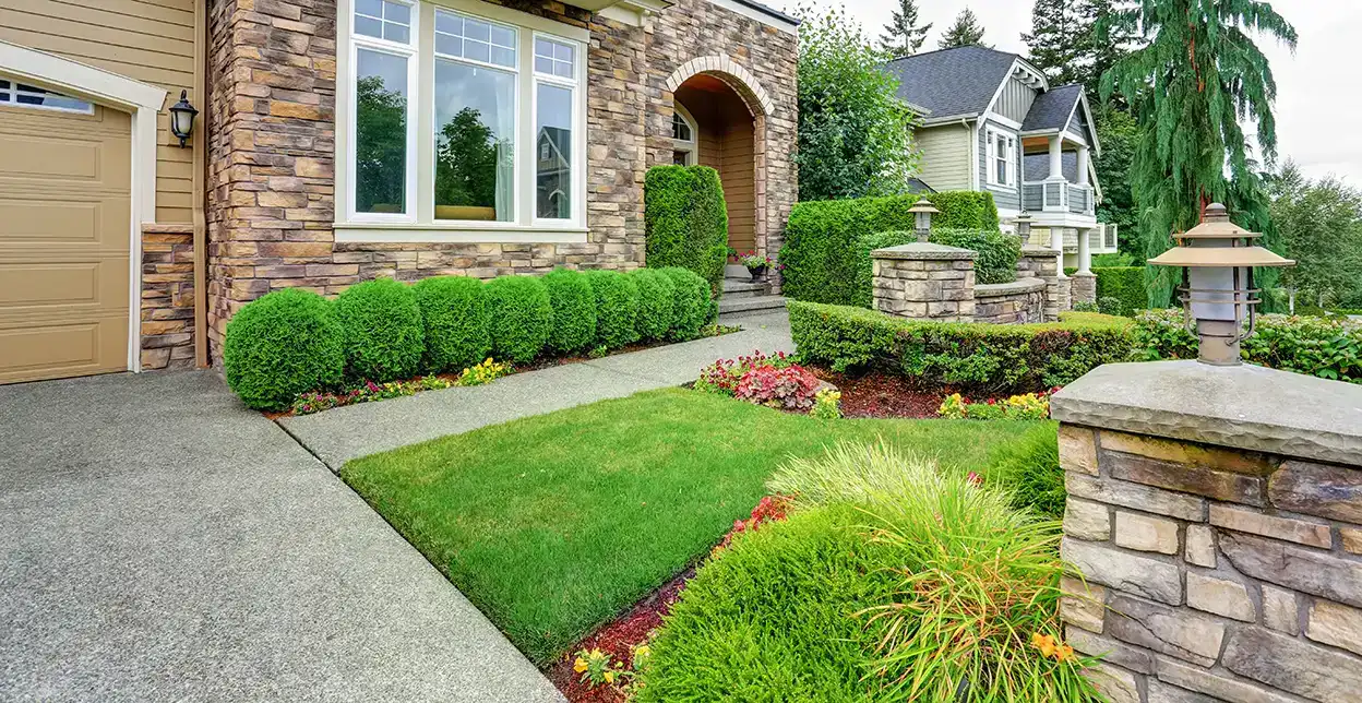 A home's front yard with stone retaining walls, outdoor lighting, expertly landscaped shrubs, and flowers planted in garden beds.