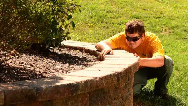 A Grounds Guys service professional adjusting a stone in a retaining wall.