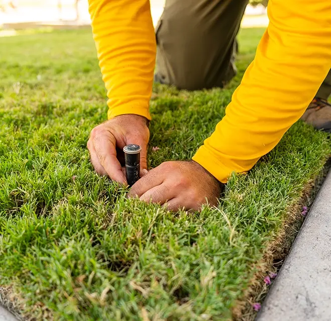 The Grounds Guys service professional adjusting a sprinkler head in the grass.