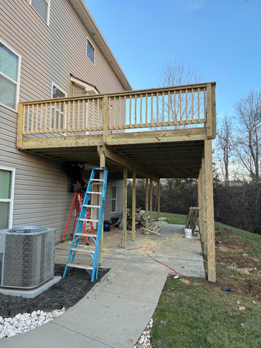 Brand new large raised deck with supports above concrete patio and basement entrance.
