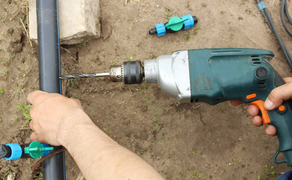 Landscaper drilling hole in drip irrigation tube