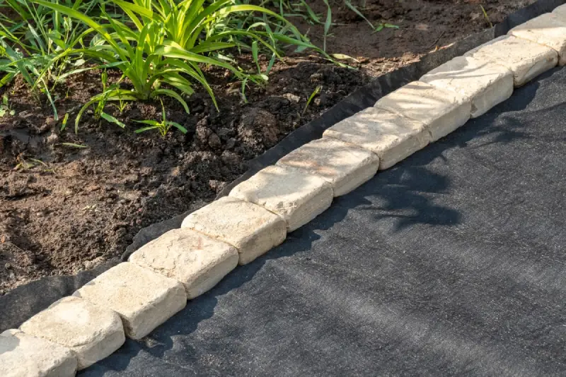 Stone garden bed edging on top of landscape fabric