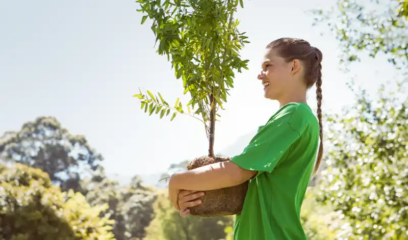 Girl smiling and wrapping arms around small tree to be planted.