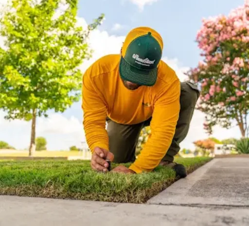 A Grounds Guys technician inspecting a sprinkler head to identify the cause of an irrigation system problem.