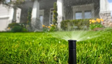 A sprinkler spraying water on the front lawn of a home.