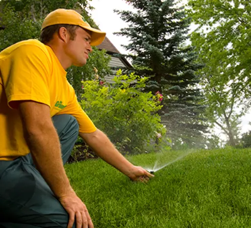 A Grounds Guys service professional inspecting and adjusting a sprinkler head in a lawn irrigation system.
