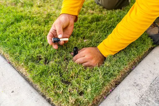 A Grounds Guys service professional repairing a sprinkler head as part of a targeted irrigation system repair.