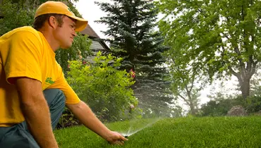 A Grounds Guys service professional inspecting and adjusting a sprinkler head in a lawn irrigation system.