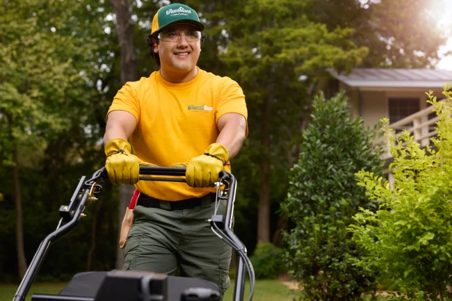A Grounds Guys associate smiling while mowing a customer's lawn.