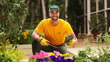 The Grounds Guys landscaping professional planting colorful annual flowers in a residential flower bed as part of seasonal landscaping and garden maintenance services.