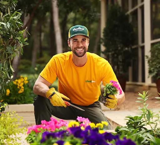 The Grounds Guys landscaping professional planting colorful annual flowers in a residential flower bed as part of seasonal landscaping and garden maintenance services.