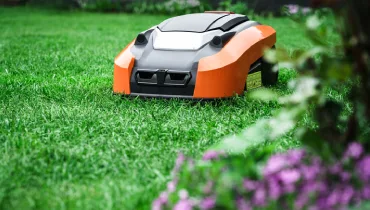 An orange and black robotic lawn mower cutting grass in a garden.