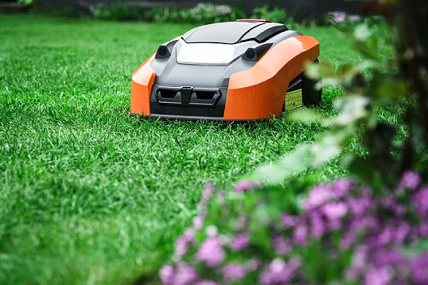 An orange and black robotic lawn mower cutting grass in a garden.