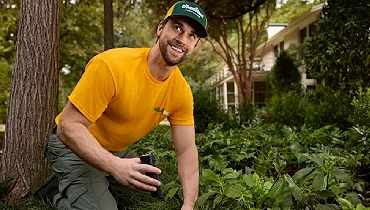 The Grounds Guys service professional kneeling in a planting bed while assessing a residential property during an irrigation evaluation.