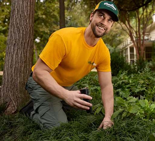 The Grounds Guys service professional kneeling in a planting bed while assessing a residential property during an irrigation evaluation.