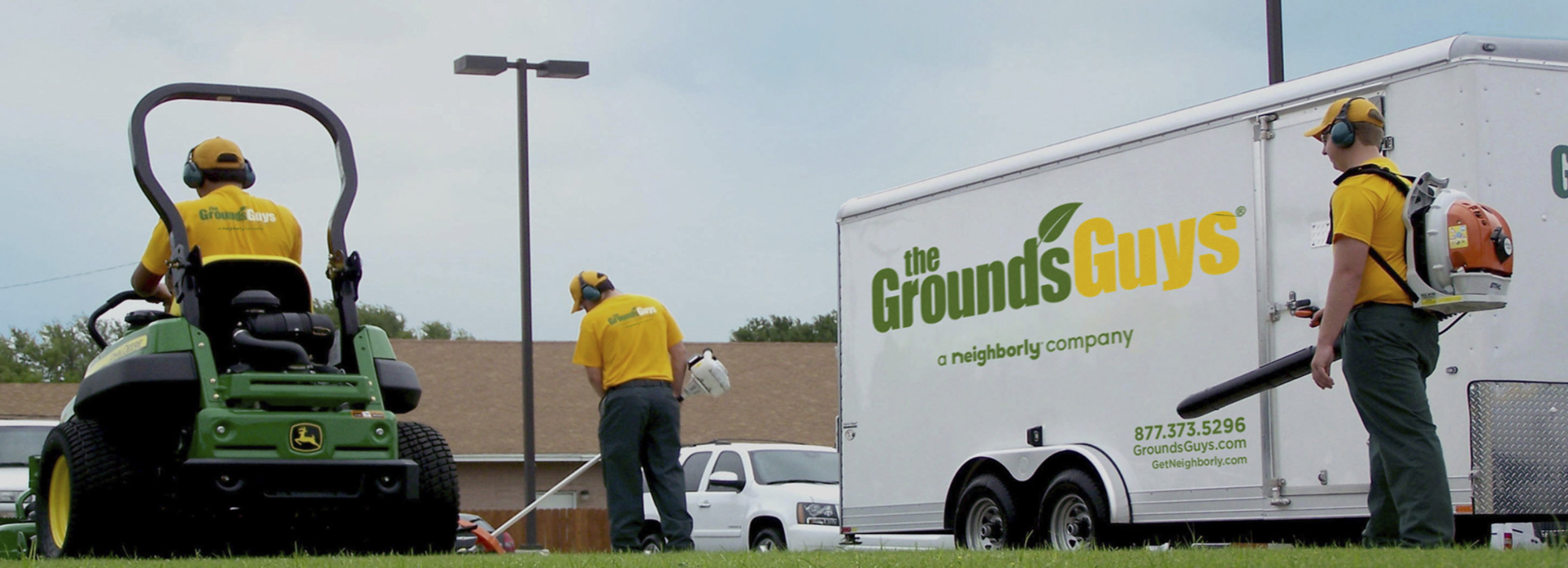 Grounds Guys crew cleaning up lawn next to company truck and trailer.