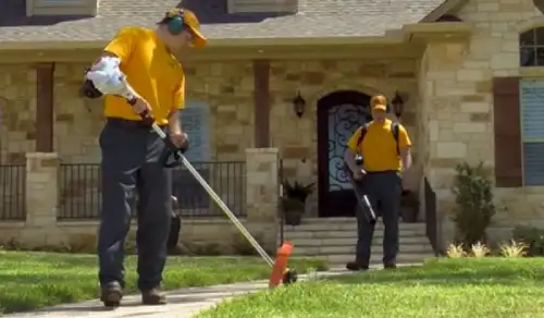 Two Grounds Guys workers performing lawn maintenance in front yard of home.