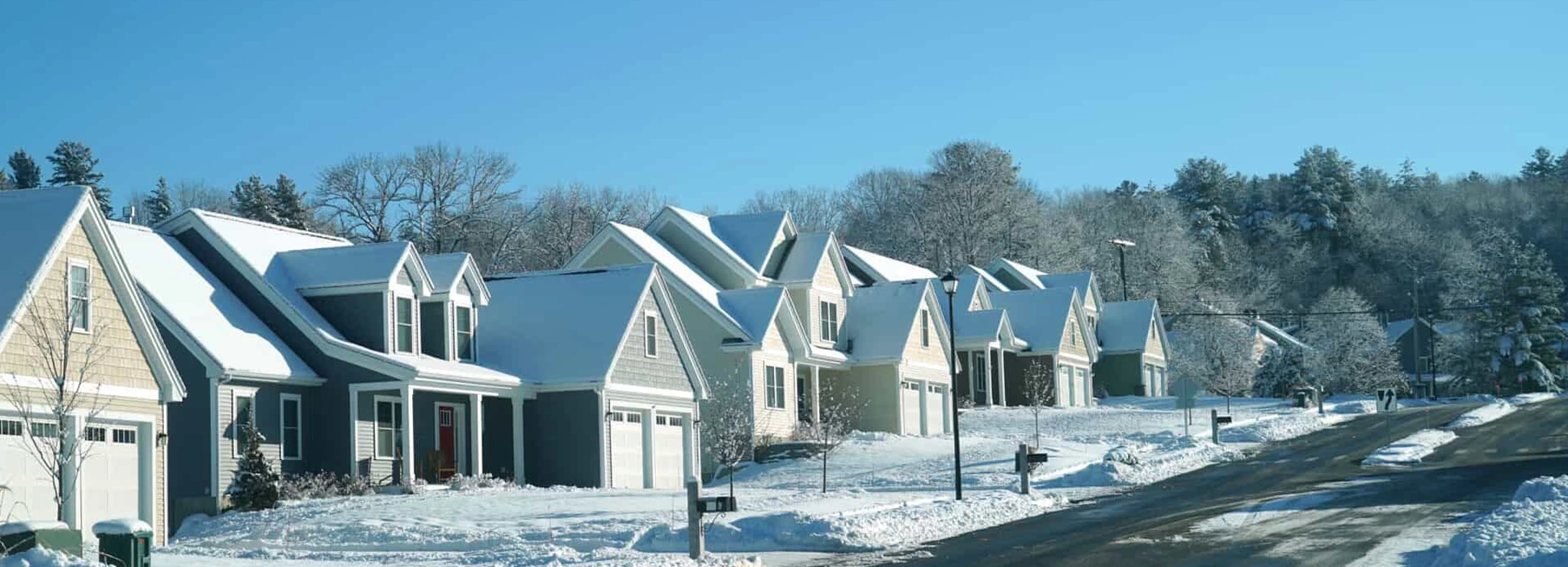 Row of residential houses on snowy hill with plowed road.