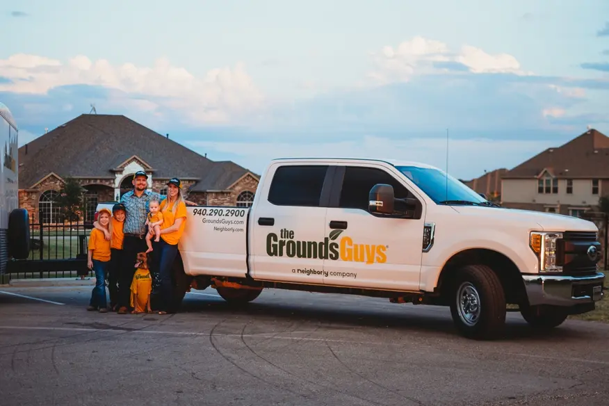 Ben and Alison Vance with their three children and dog standing beside The Grounds Guys branded pickup truck.
