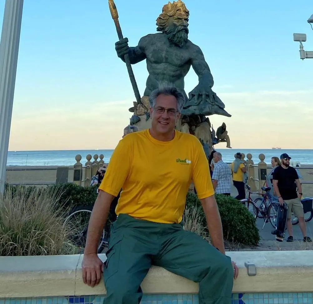 Todd Antonick at Virginia Beach boardwalk with statue of Neptune in background.
